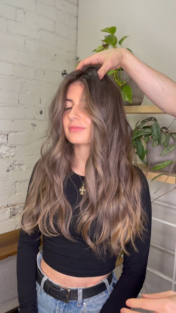 Long dark blonde waves with caramel highlights displayed as a hand lifts the crown