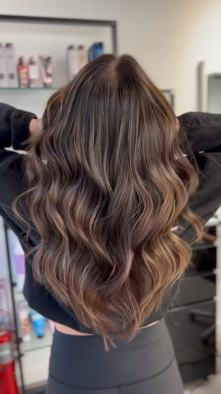 Glossy brunette hair with honey highlights styled in large, loose curls