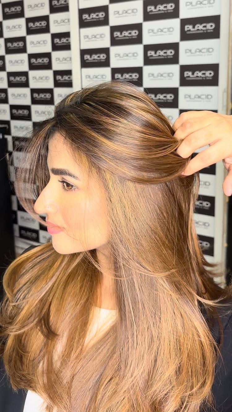 Long highlighted layers fall over a woman’s shoulders as a hand lifts her hair