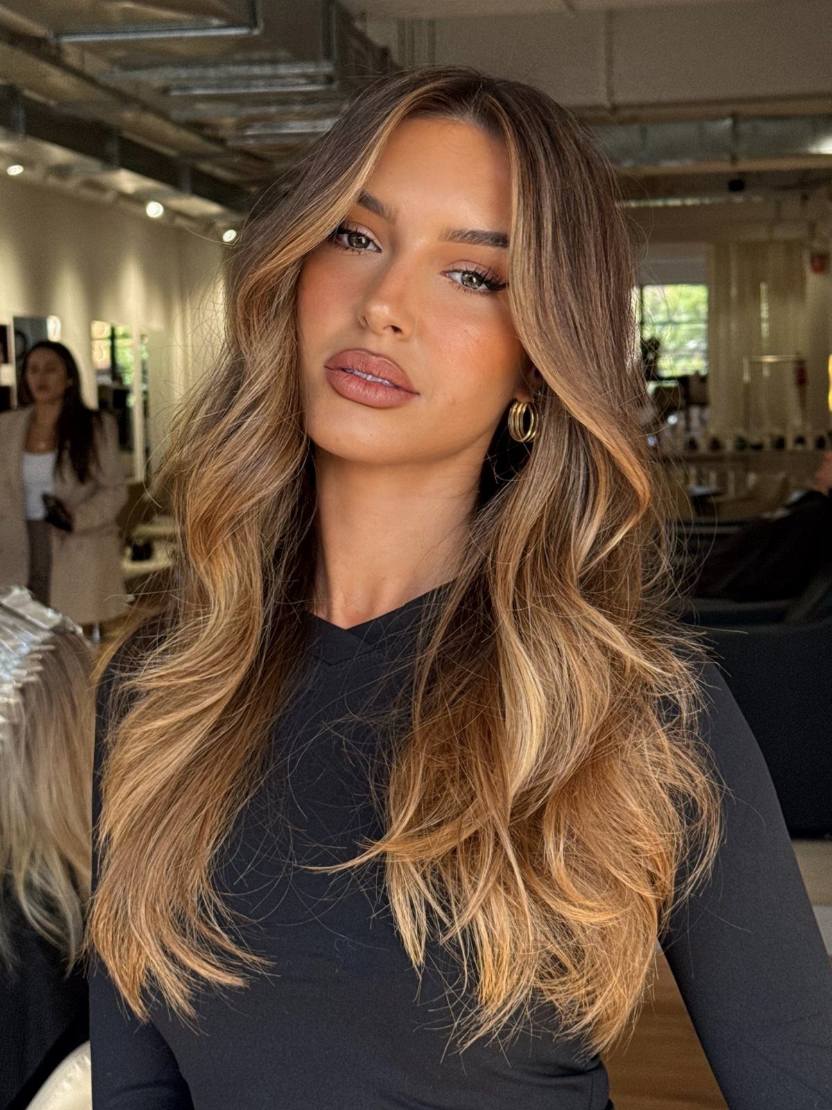 Woman with long, softly waved chestnut hair and warm caramel highlights