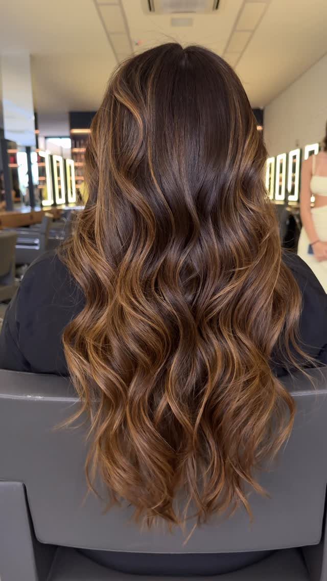 Long dark brown waves with blended caramel highlights in a salon