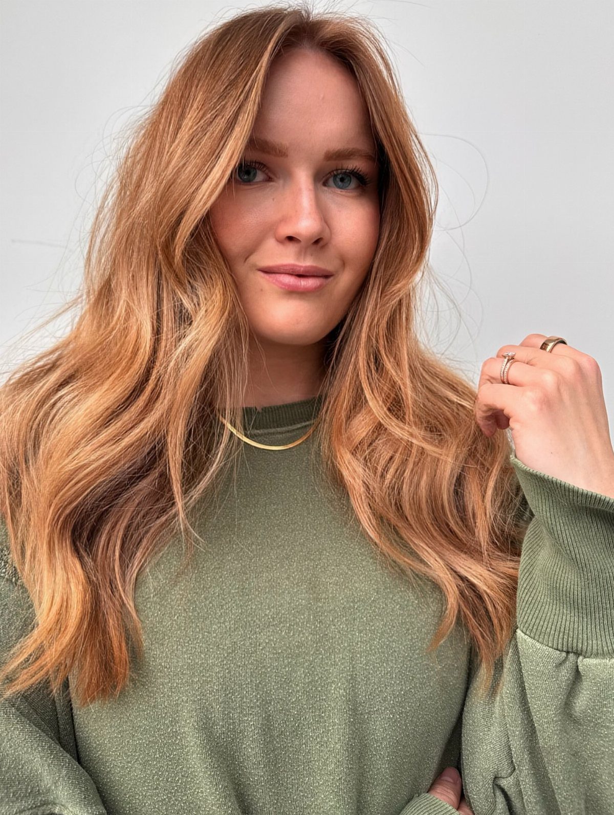 Woman with long wavy dark strawberry-blonde hair and subtle darker roots