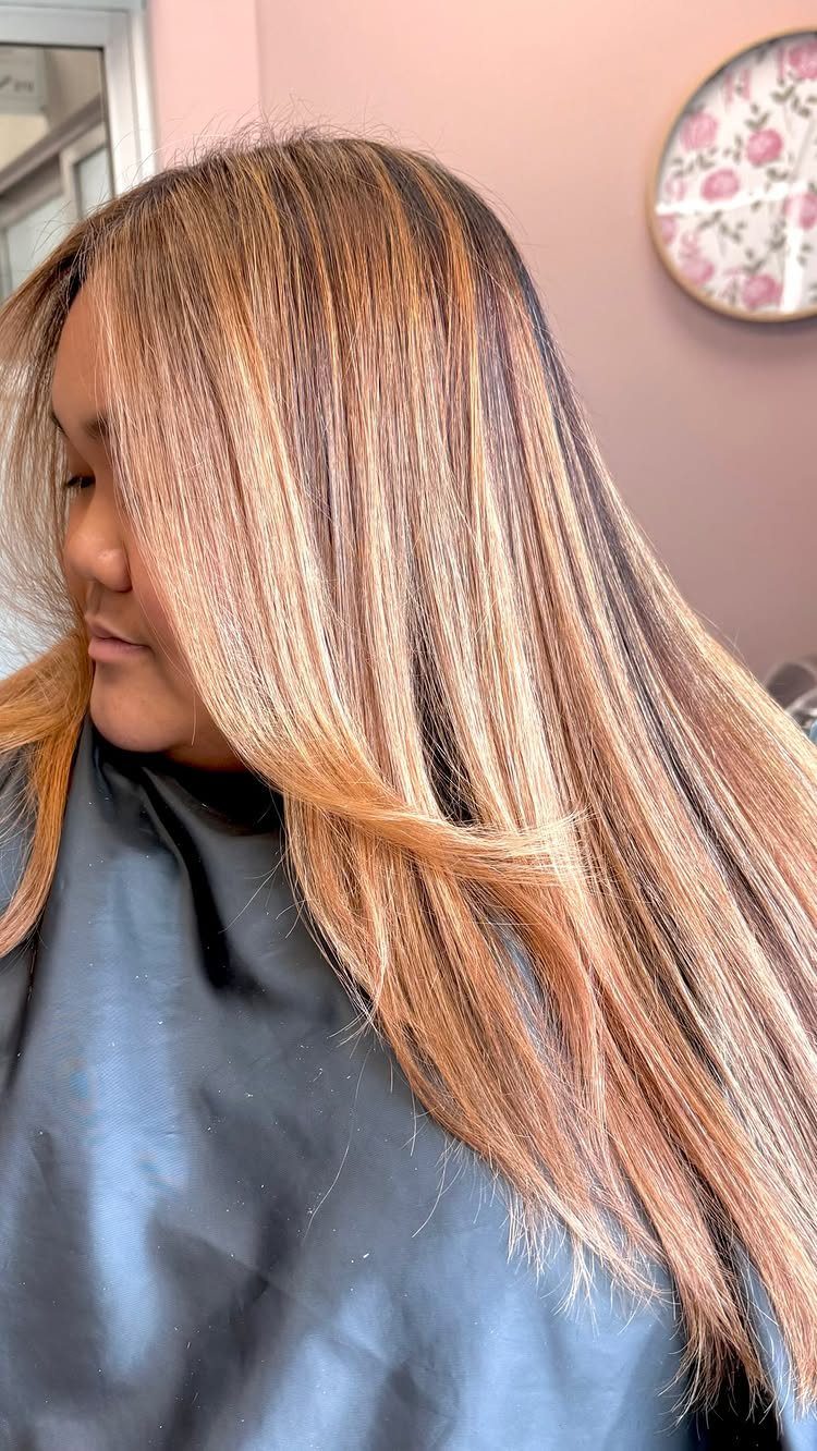 Long strawberry blonde hair with honey-gold highlights draped over a dark salon cape