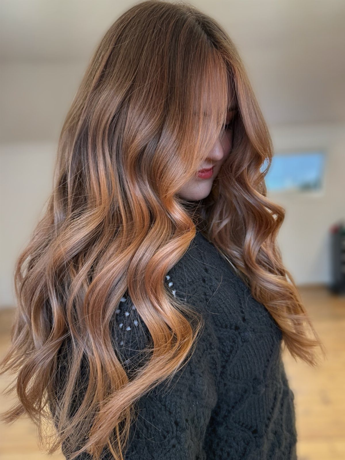 Woman with long waves and warm strawberry-blonde highlights wearing a black knit sweater