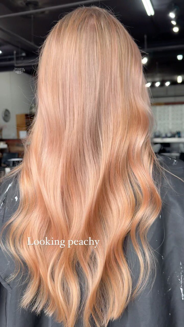 Long pastel strawberry-blonde waves with delicate peach-pink tones in a salon