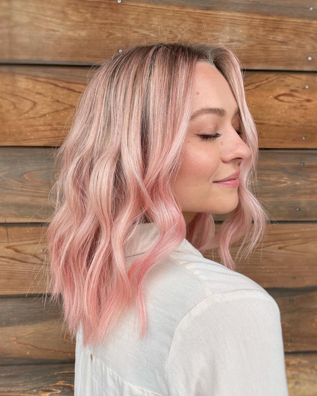 Woman with wavy blonde hair tinted pastel pink against a wooden wall