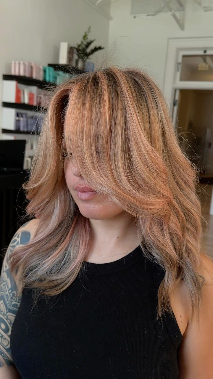 Woman with long peach blonde layers and warm highlights in a salon