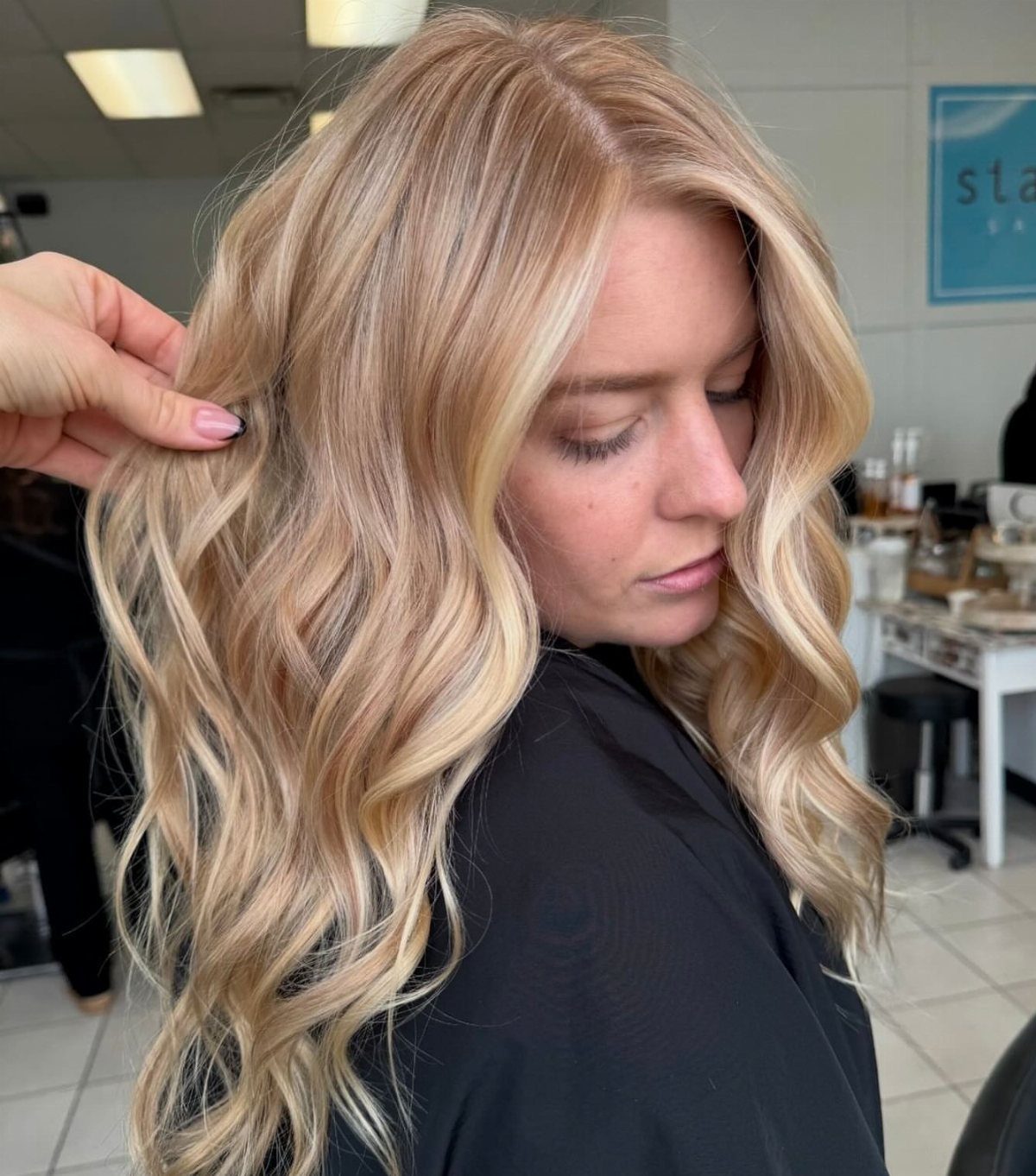Woman with long, wavy blonde hair featuring warm strawberry and pale highlights in a salon.