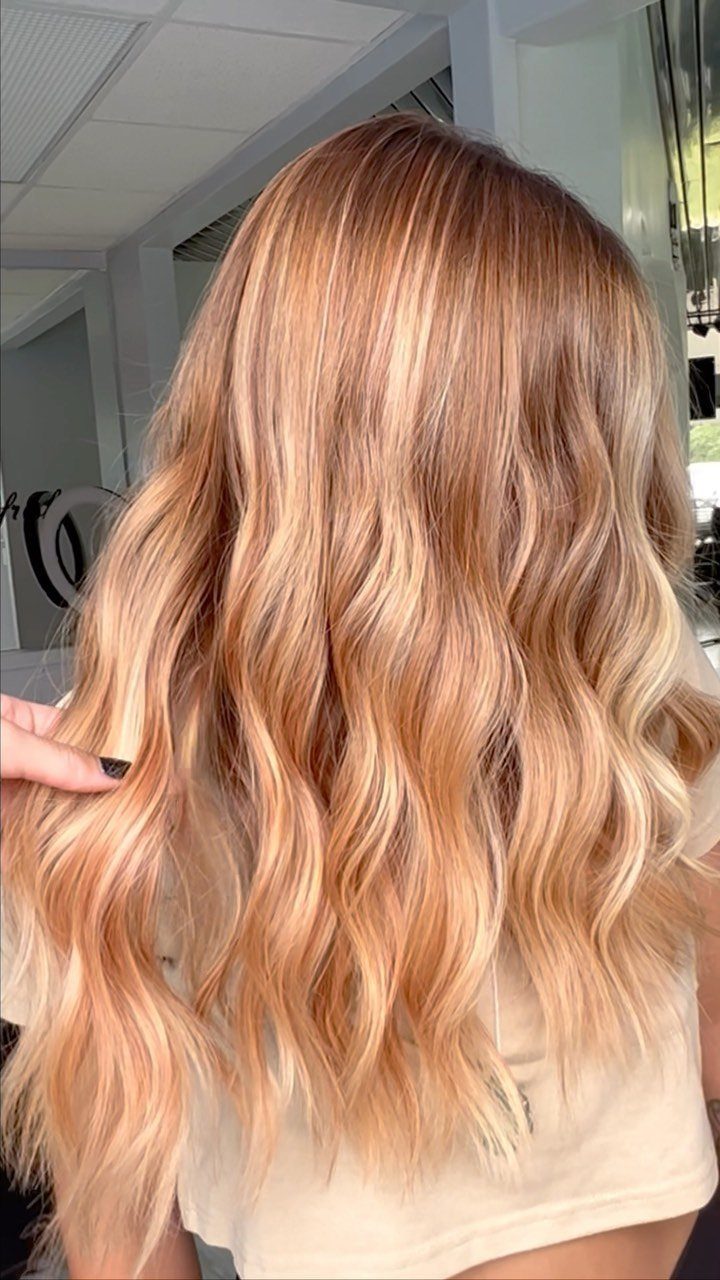 Long strawberry blonde waves show softly blended lighter highlights and darker roots