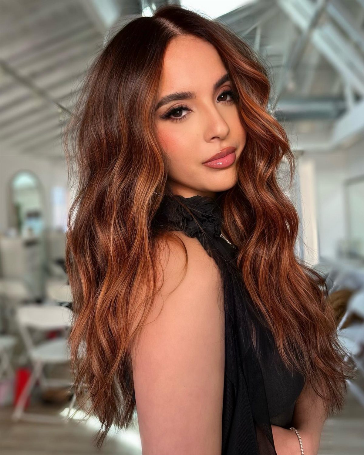 Woman with long wavy brunette hair highlighted with warm copper and auburn tones