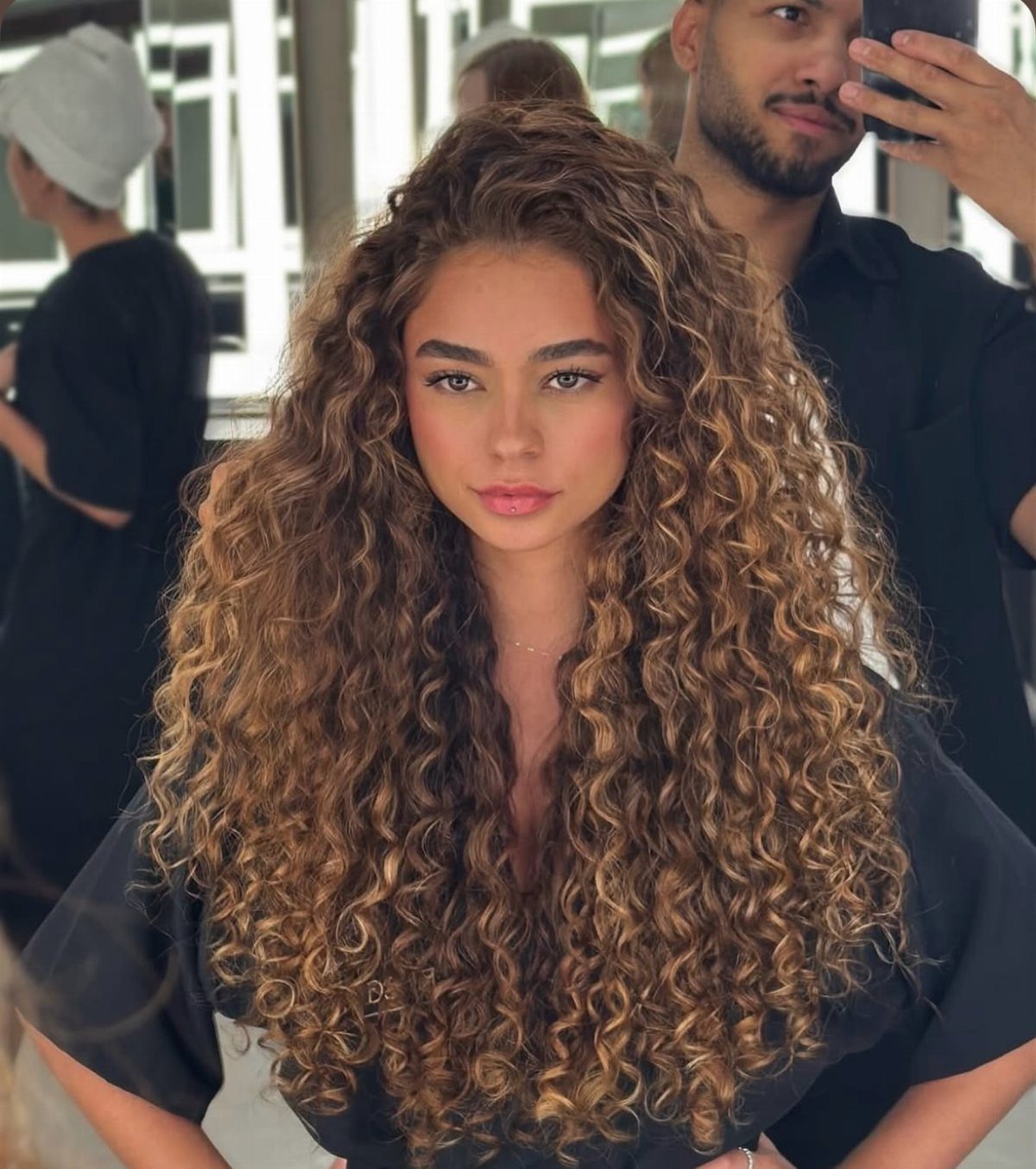 Woman displaying long brown curls with dimensional balayage highlights in a salon