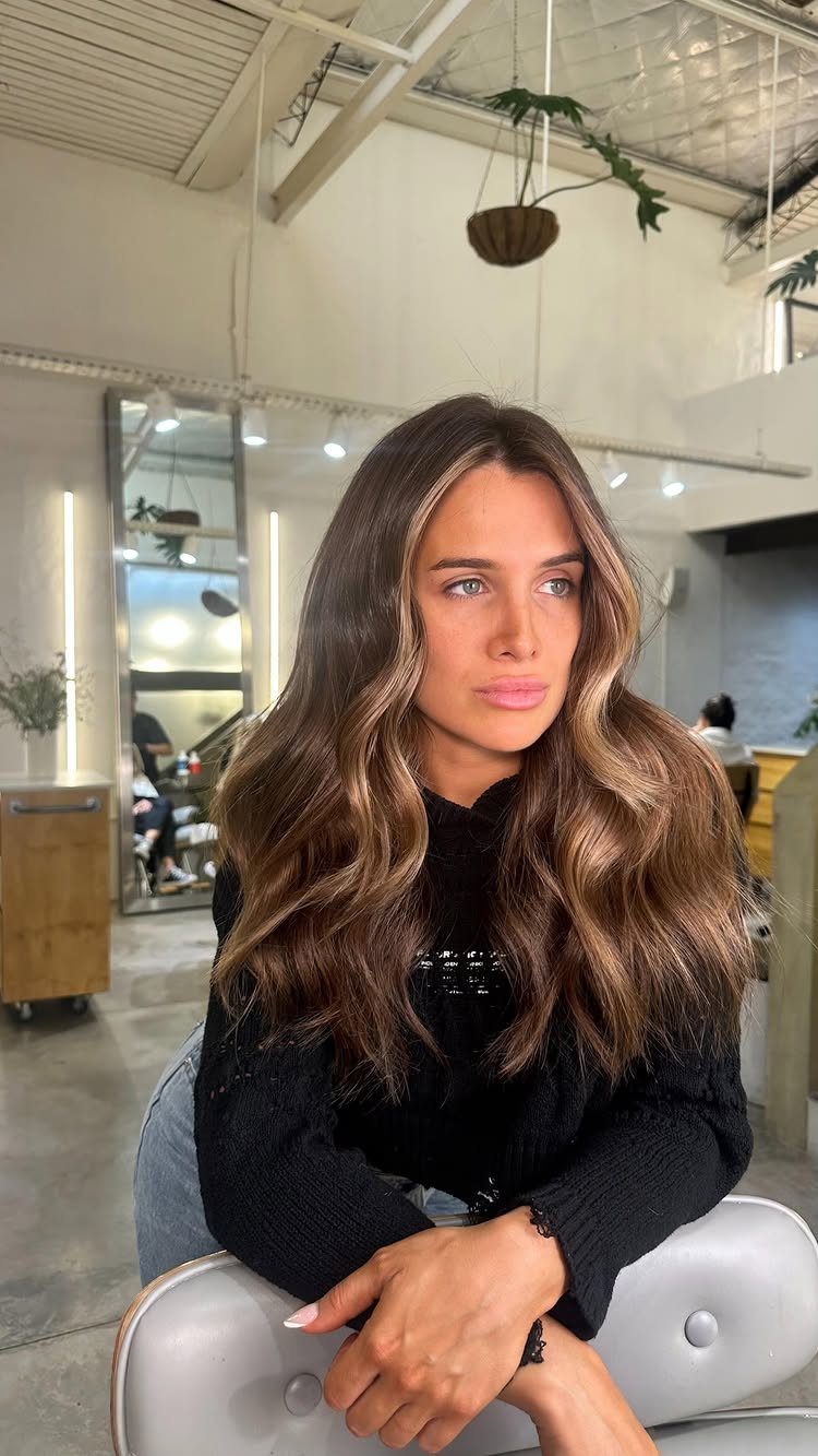 Woman with wavy brown hair and lighter face-framing strands seated in a salon