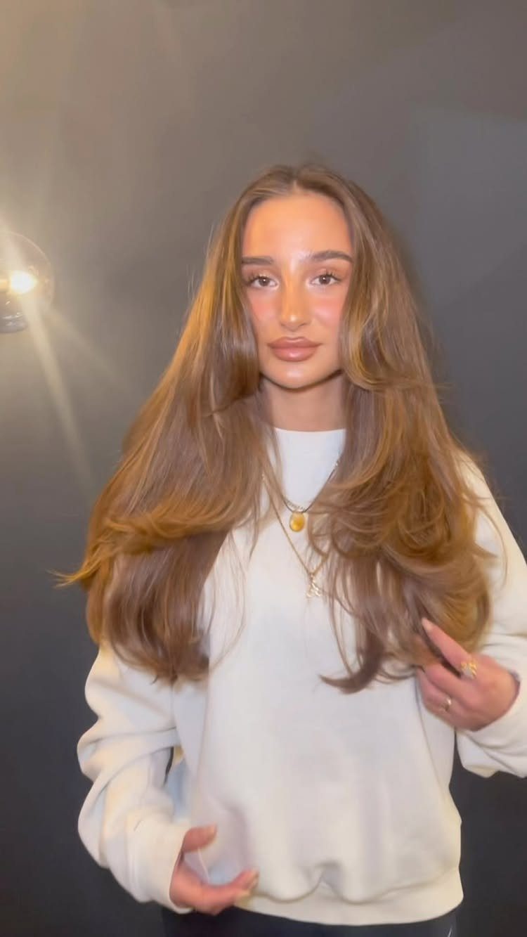 Woman with long, softly highlighted brunette hair wearing a white sweatshirt