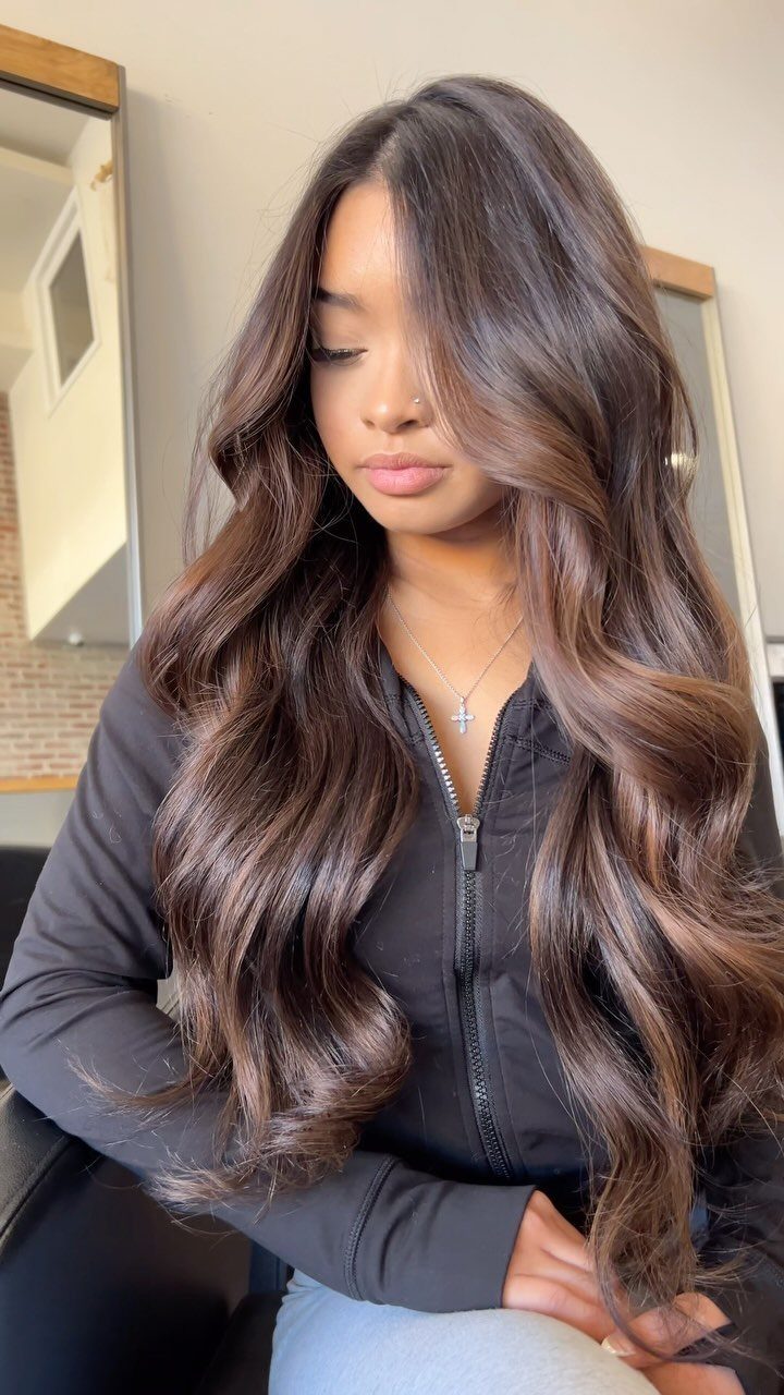 Woman displaying long wavy brown hair with warm softly blended sun-kissed balayage highlights