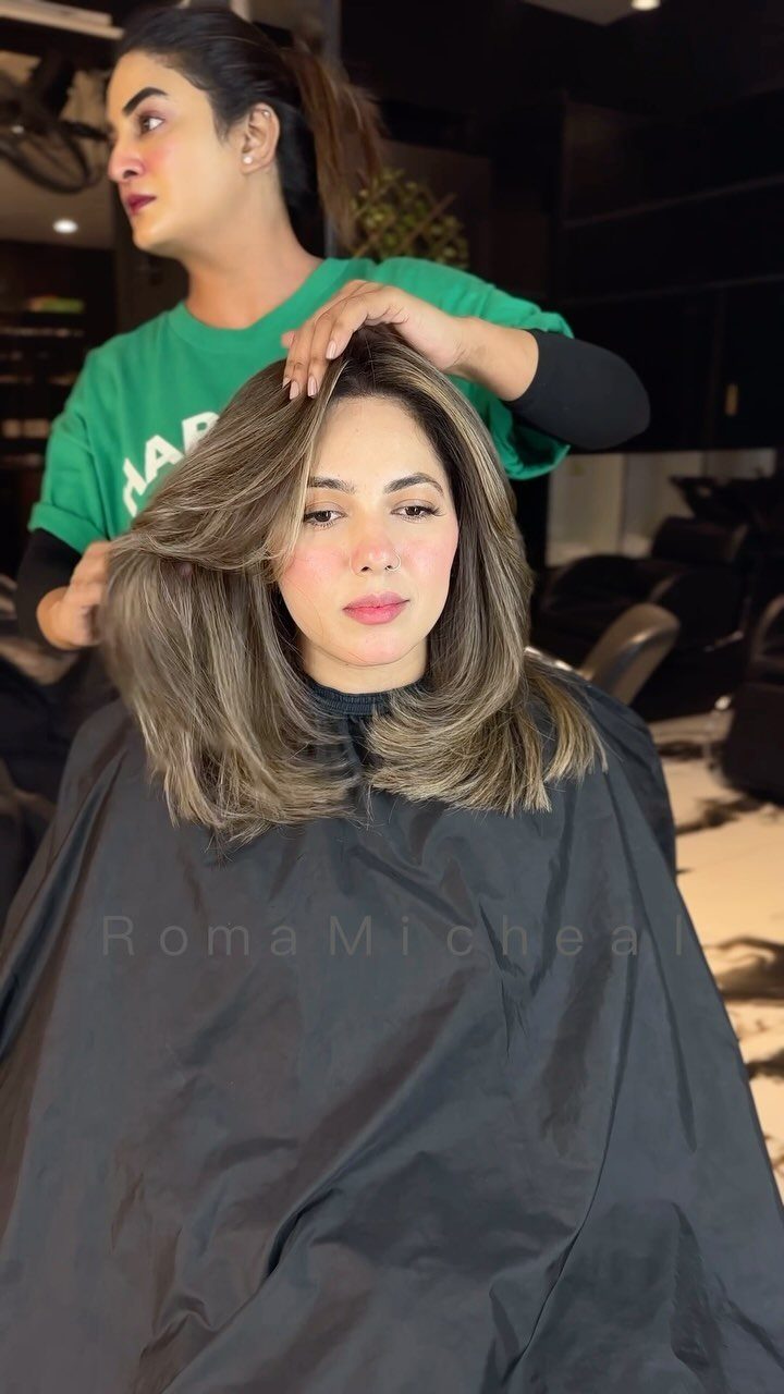 Brown-haired woman displays layered hair with warm bronze highlights in a salon