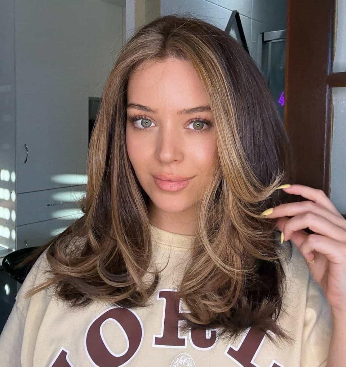 Woman with layered brown hair and caramel highlights framing her face