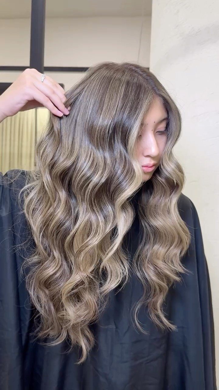 Wavy brown hair with soft beige-blonde highlights shown over a black salon cape