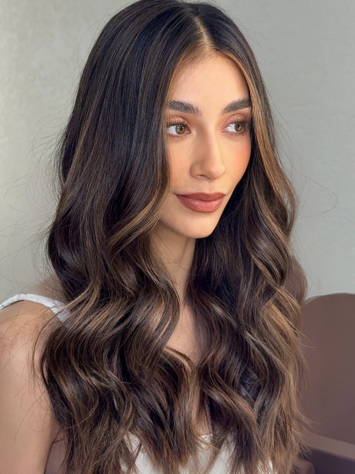 Woman with long wavy brown hair and subtle caramel brushlight highlights