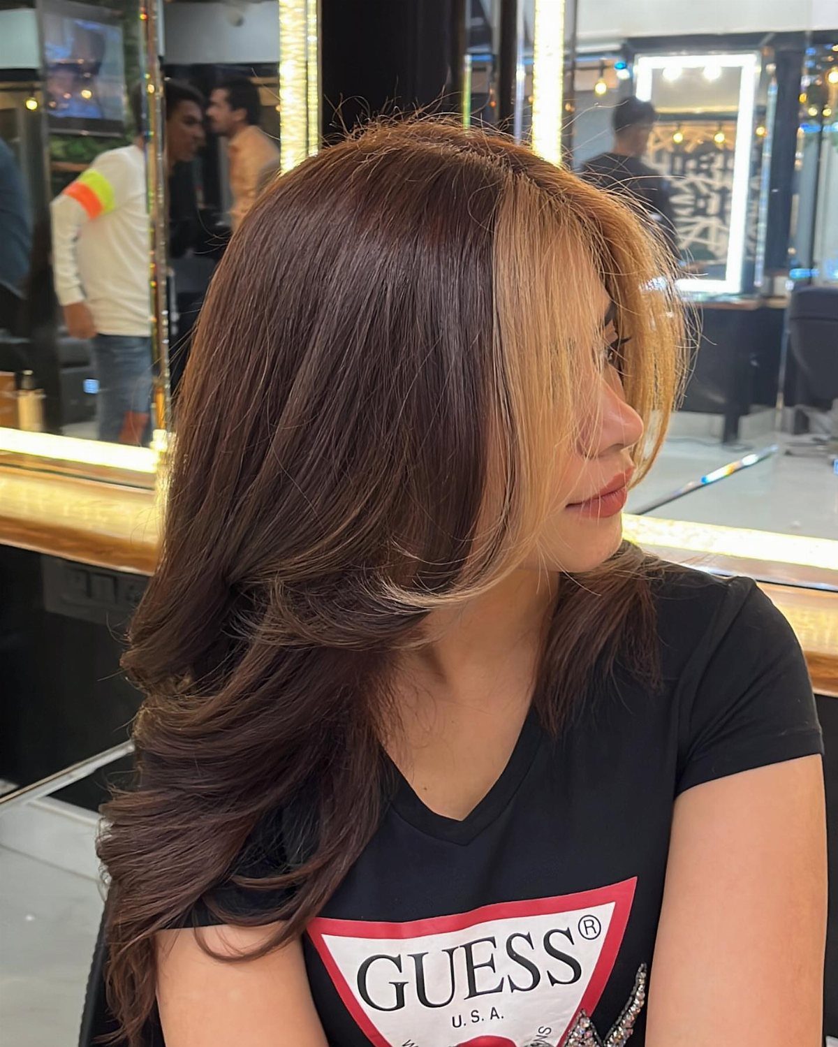 Woman showing long brown hair with caramel-blonde face-framing highlights in a salon