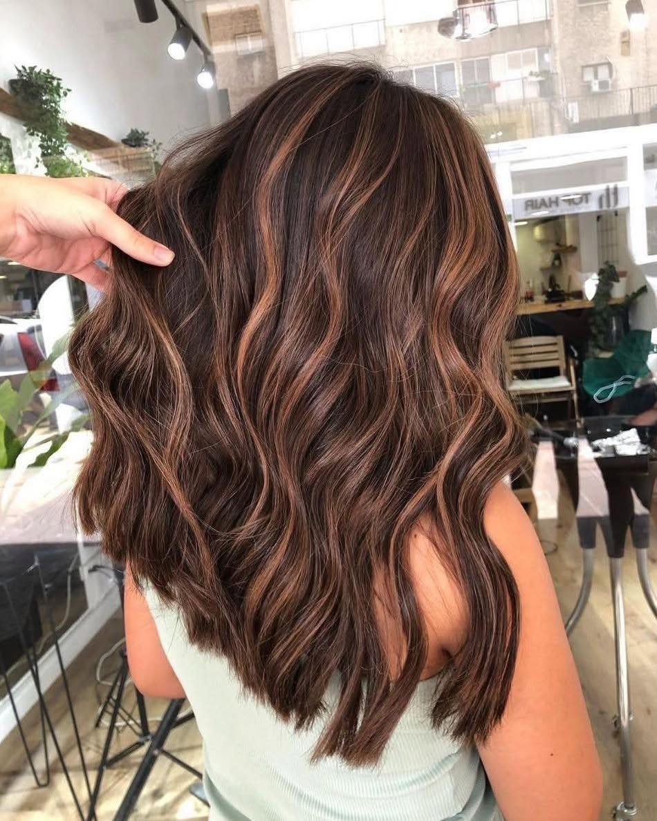 Long chocolate-brown waves with fine caramel teasylights shown in a salon