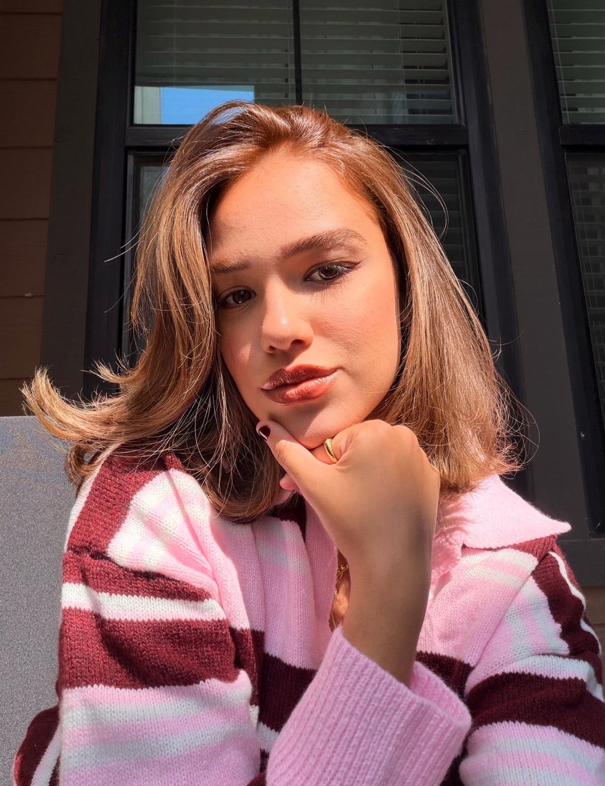 Woman with long brown waves and warm amber highlights wearing a striped sweater
