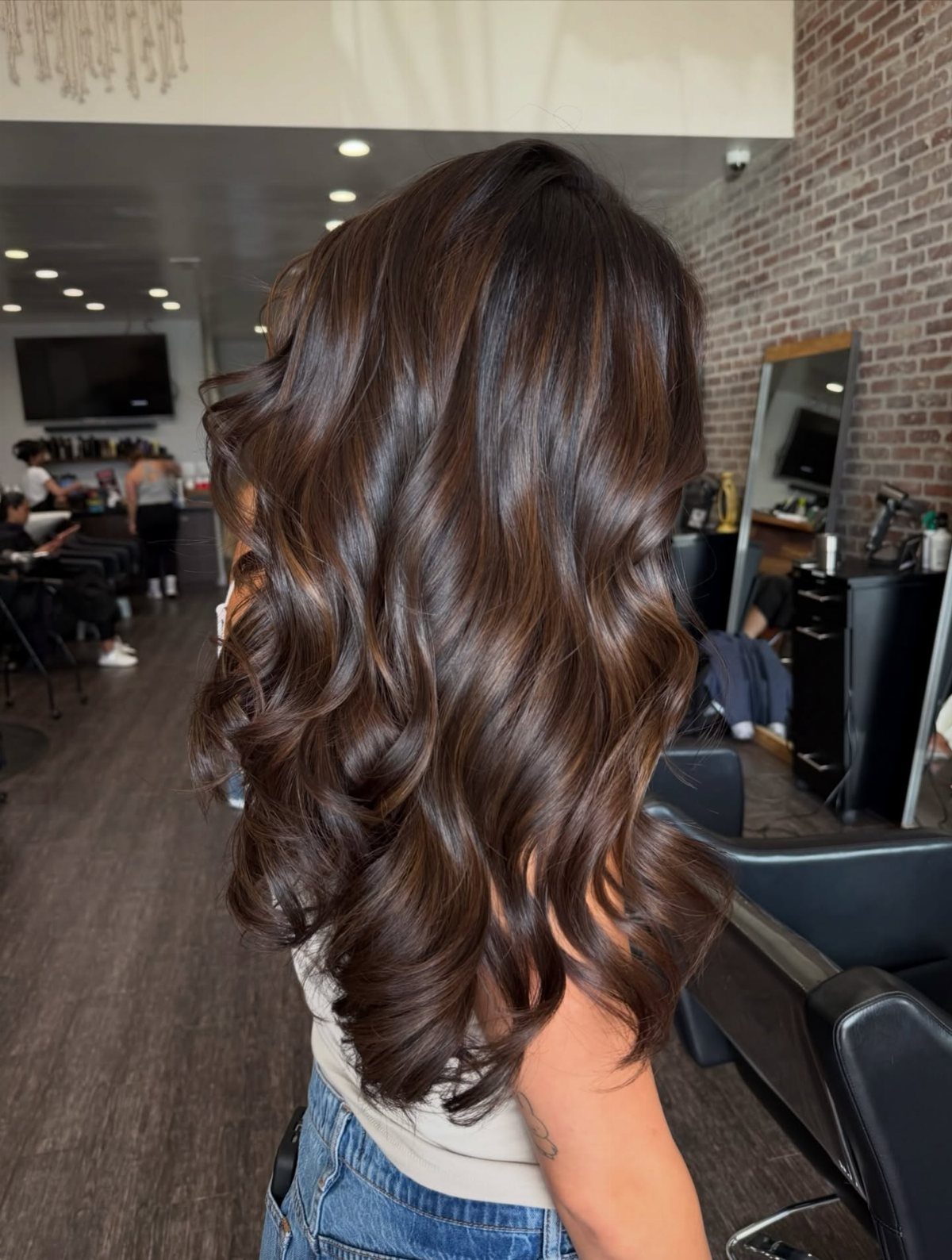 Glossy dark brown curls with subtle caramel highlights and dark roots