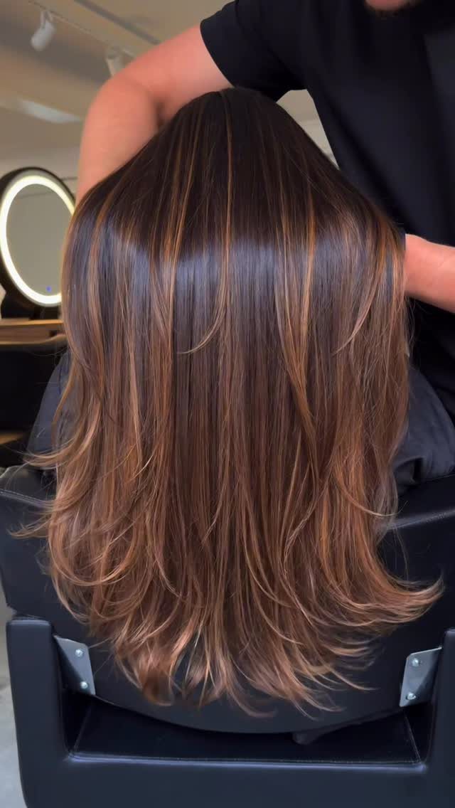 Dark brown layered hair with fine caramel highlights in a salon