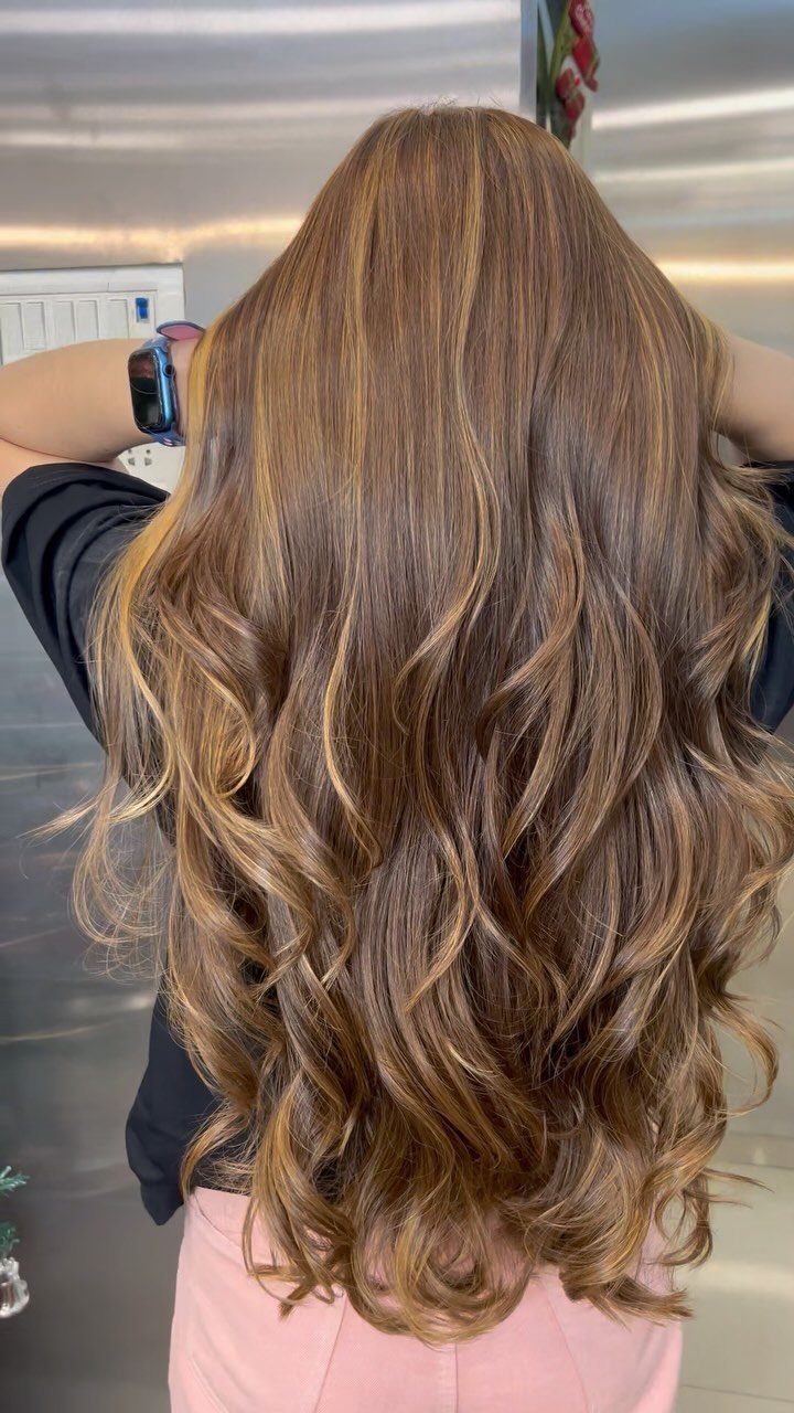 Long wavy brown hair with subtle caramel highlights and layered curls