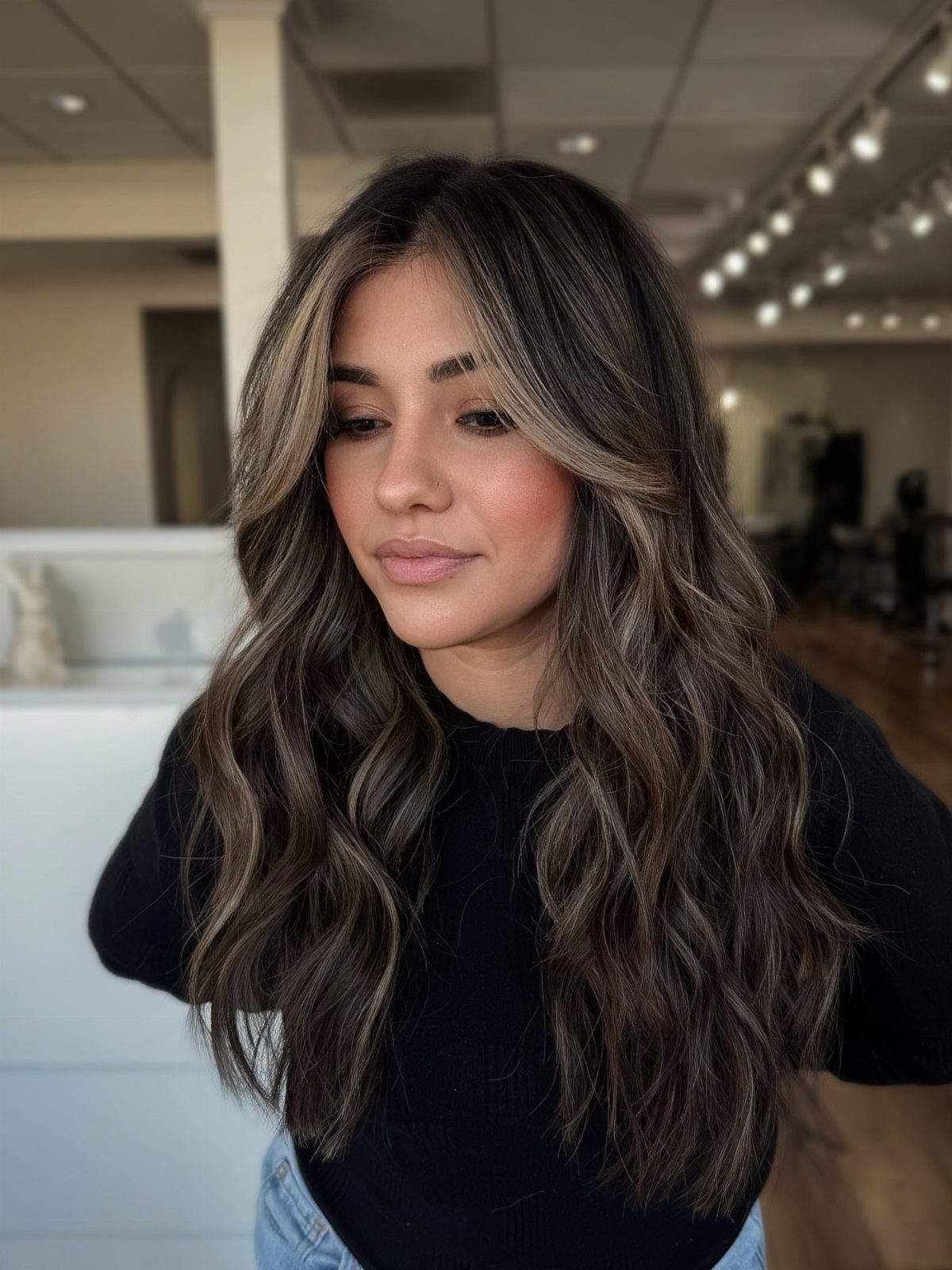 Woman showing long brunette waves with soft ash-gray beige balayage highlights