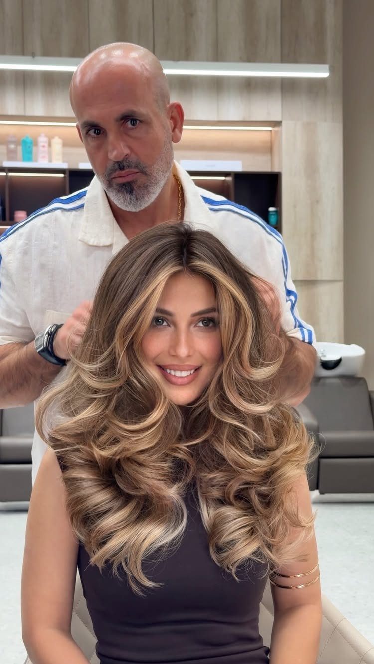 Woman displaying long brunette curls with soft beige-blonde highlights in a salon