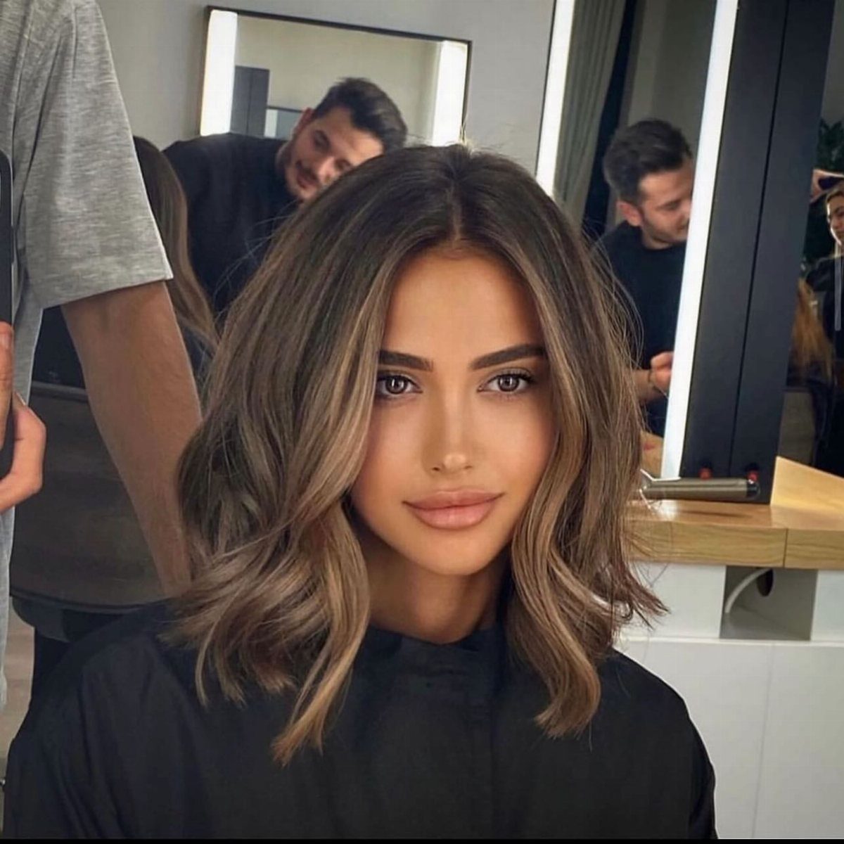 Woman showcasing a shoulder-length brunette lob with blended blonde highlights in a salon