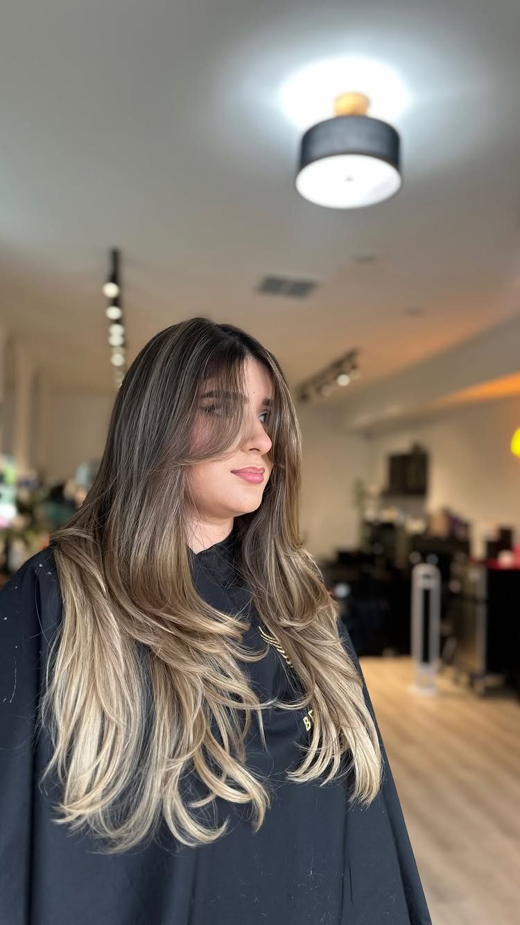 Woman displaying long brunette hair with cool blonde highlights and rounded wavy ends