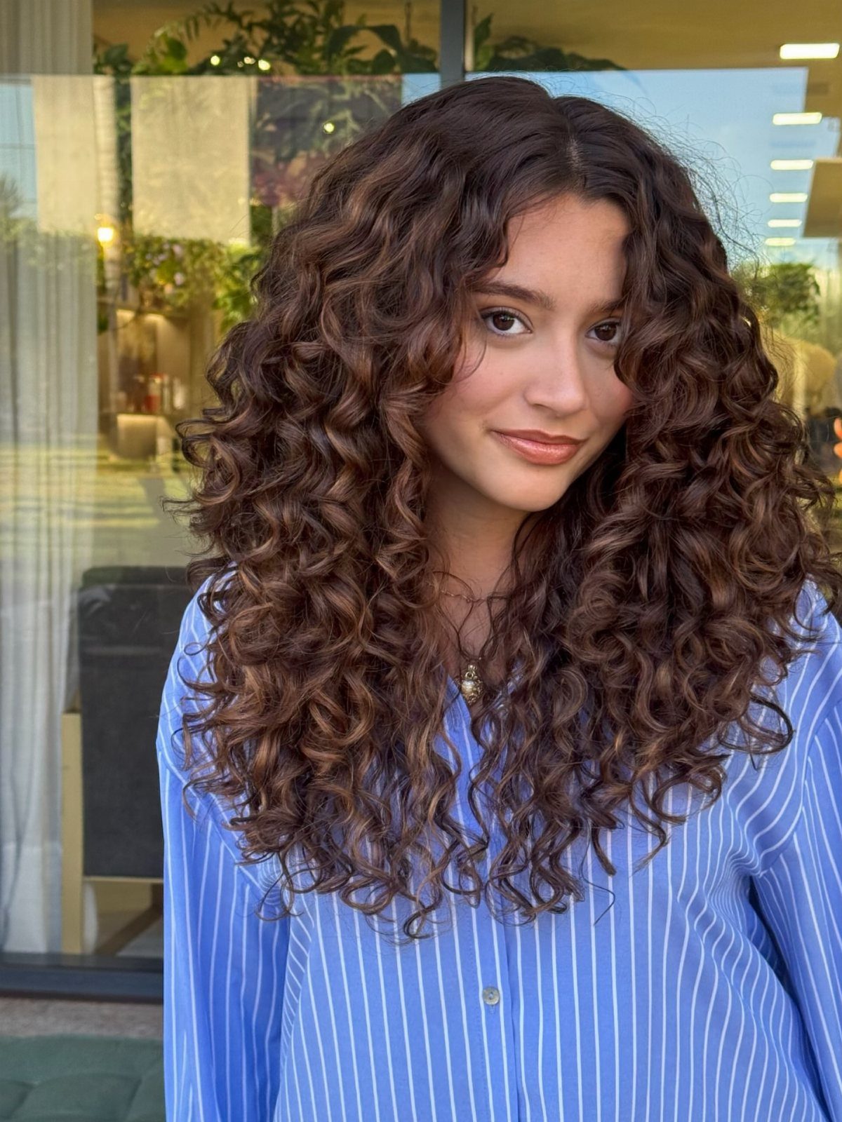 Brunette woman showing defined curly hair with subtle warm balayage highlights