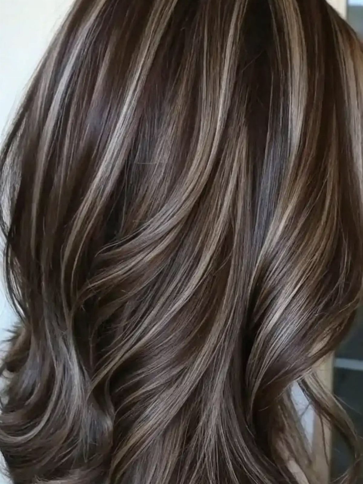 Layered brunette hair with cool gray and blonde highlights in soft waves