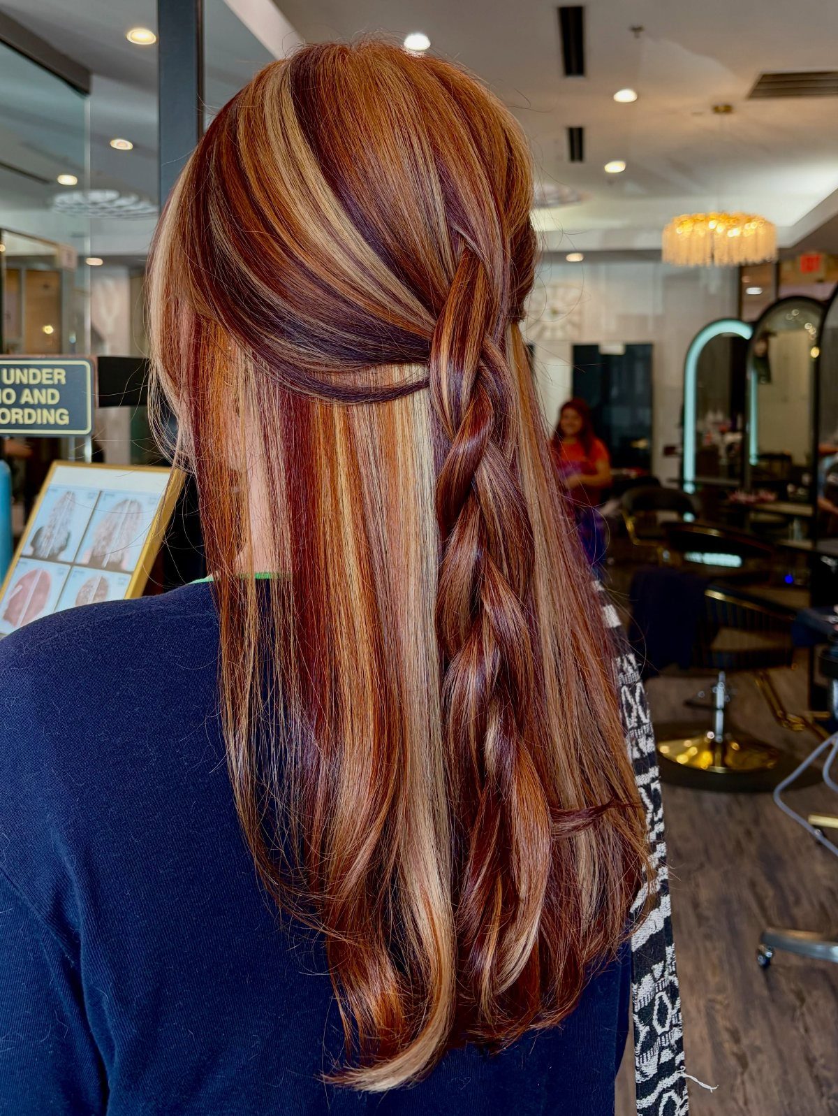 Long reddish-brown hair with chunky blonde highlights styled in a half-up braid