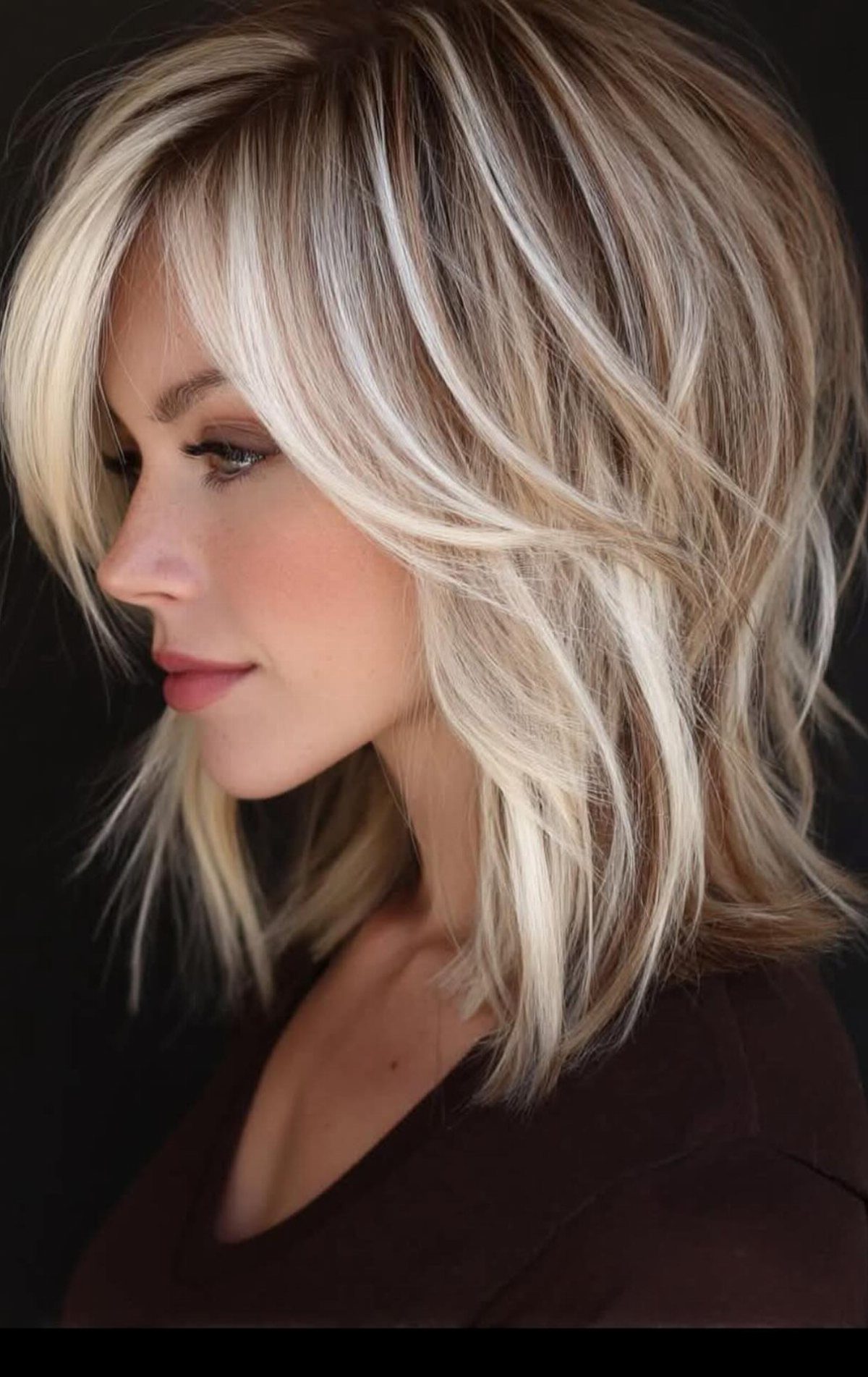 Woman with a layered angled bob and thick blonde streaks against a dark background