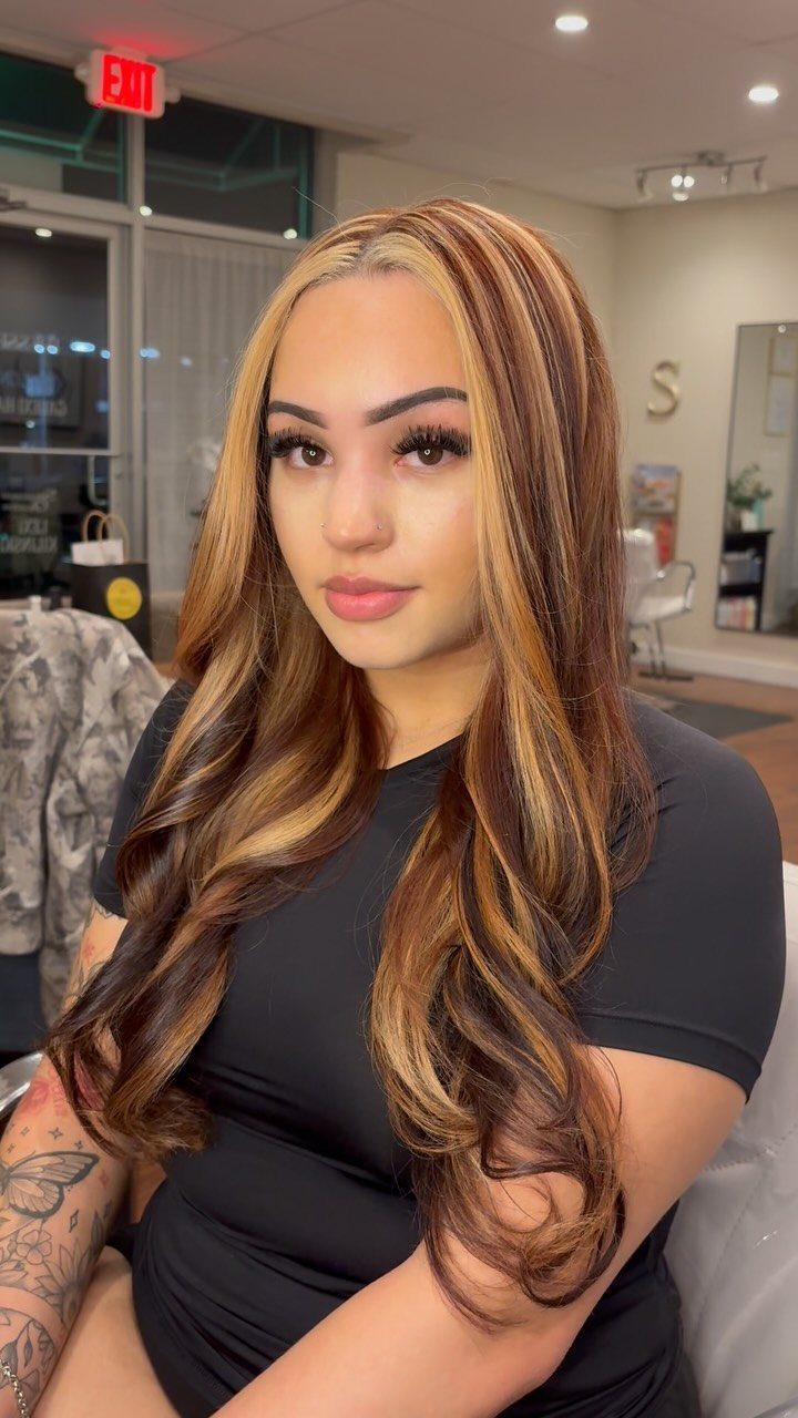Woman displaying long brown curls with chunky blonde highlights in a salon