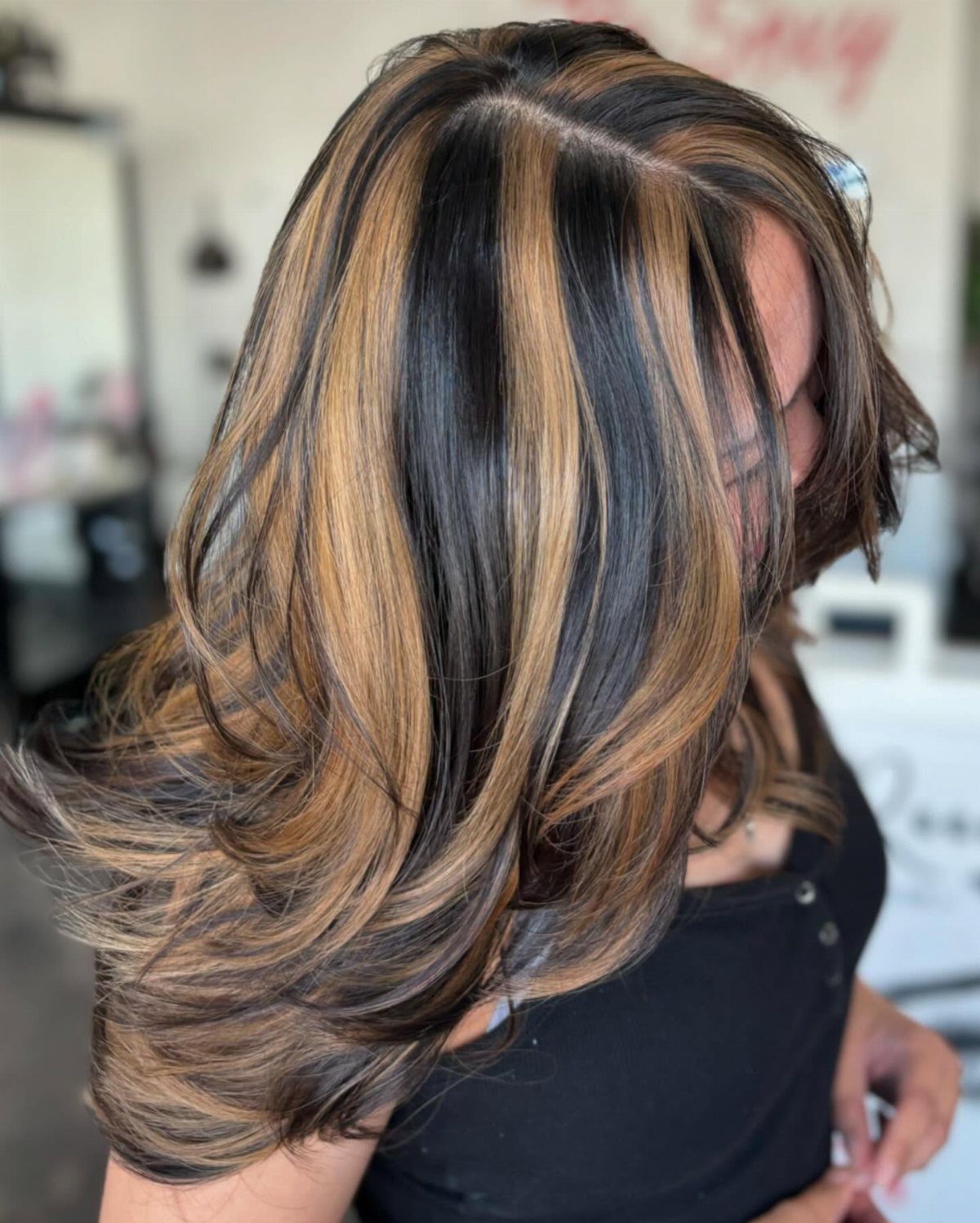 Layered dark hair with chunky blonde highlights curled into feathered ends