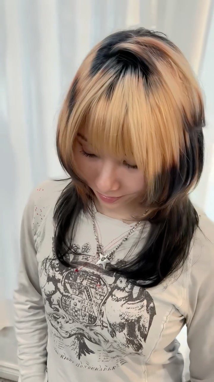 Woman with broad golden blonde highlights over dark hair and sweeping bangs
