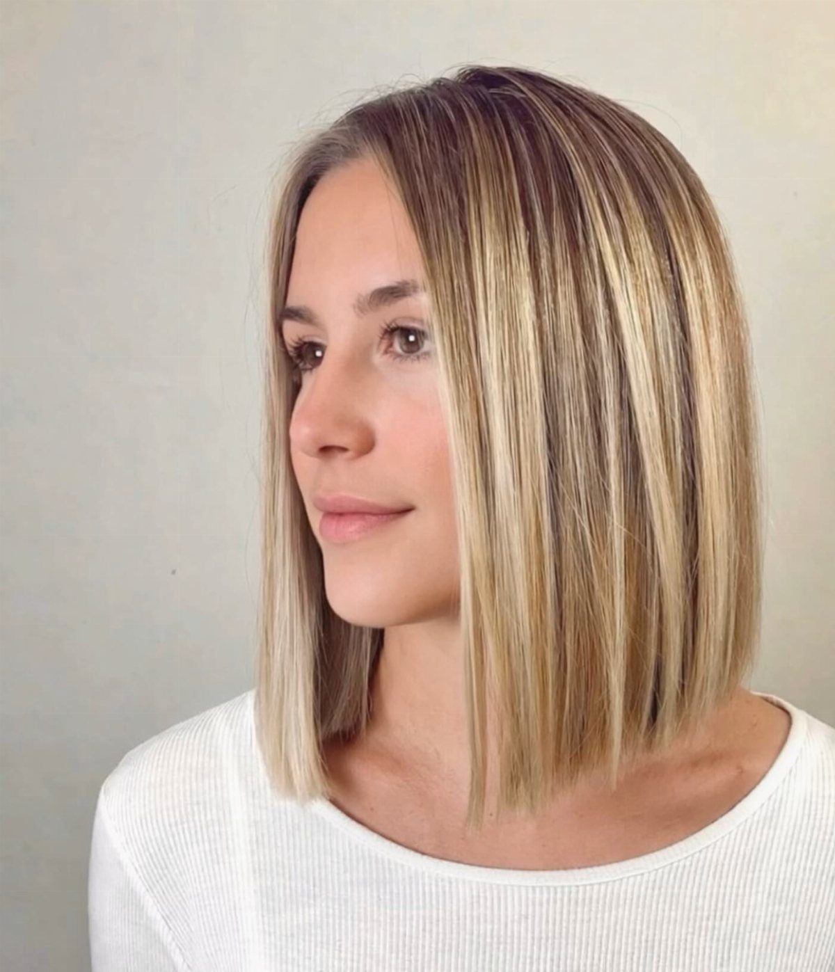 Woman with a blunt bob and subtle blonde highlights against a pale wall