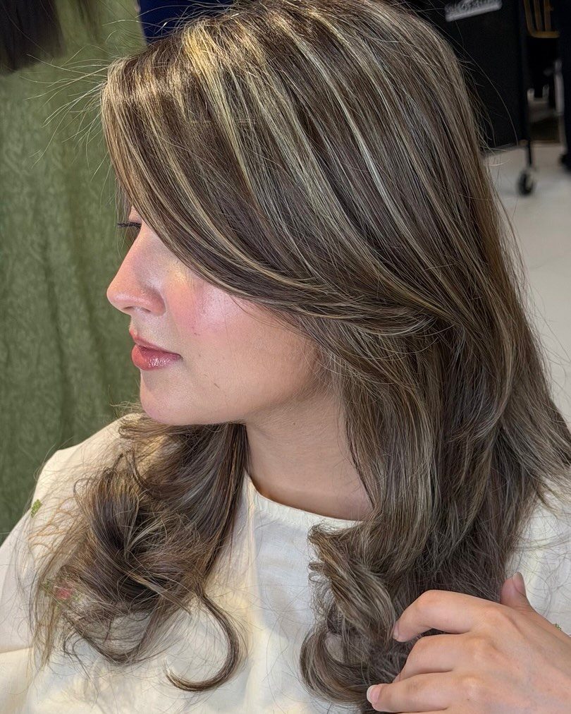 Long curled brown hair with broad blonde and darker lowlight sections in a salon