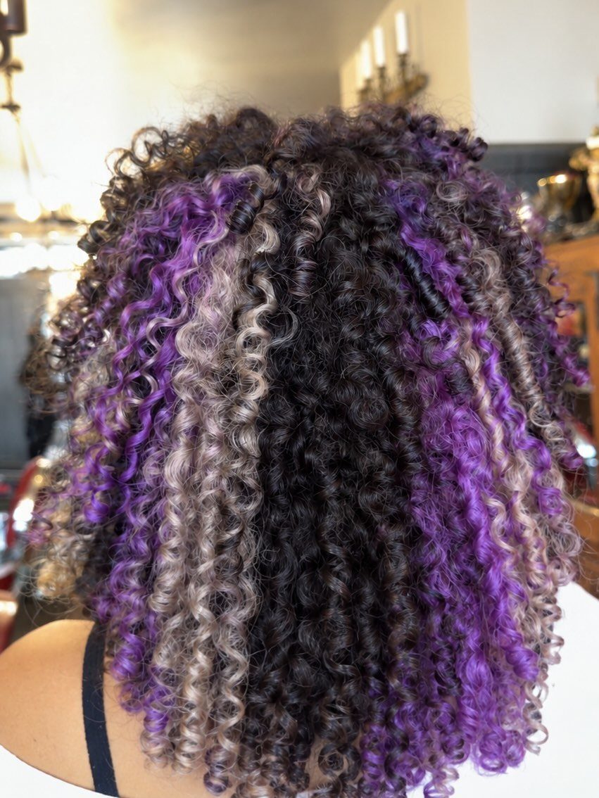 Curly dark hair with chunky purple and silver-gray highlights in a salon