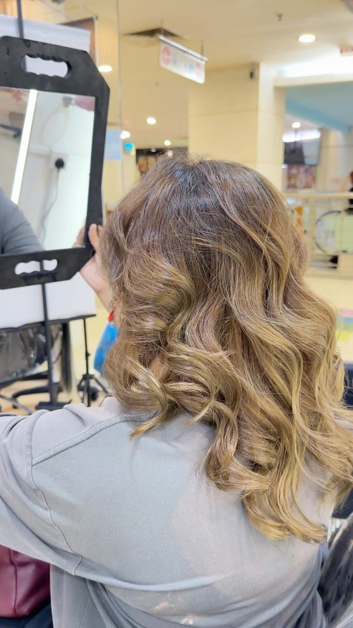 Long curled brown hair fades softly into muted ash-blonde ends in a salon