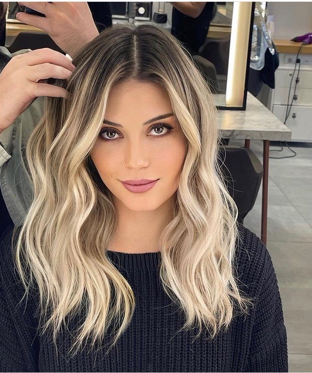Woman with dark roots and wavy champagne-blonde ombre hair in a salon