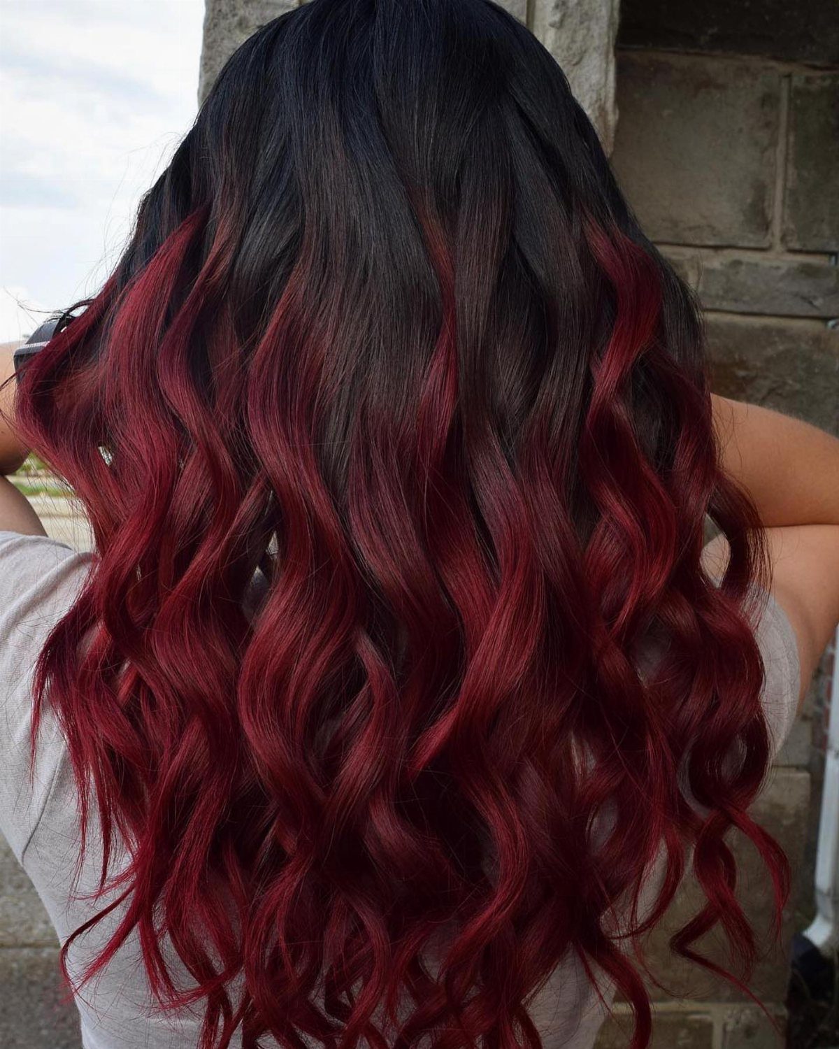 Wavy dark hair transitions into deep burgundy red ombre ends