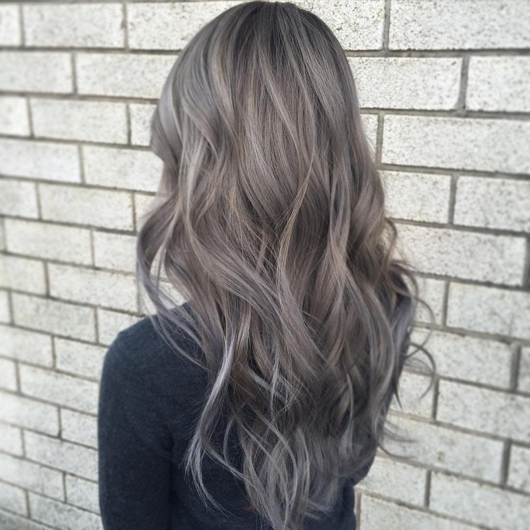 Wavy brunette hair blending into soft gunmetal-gray lengths against a brick wall