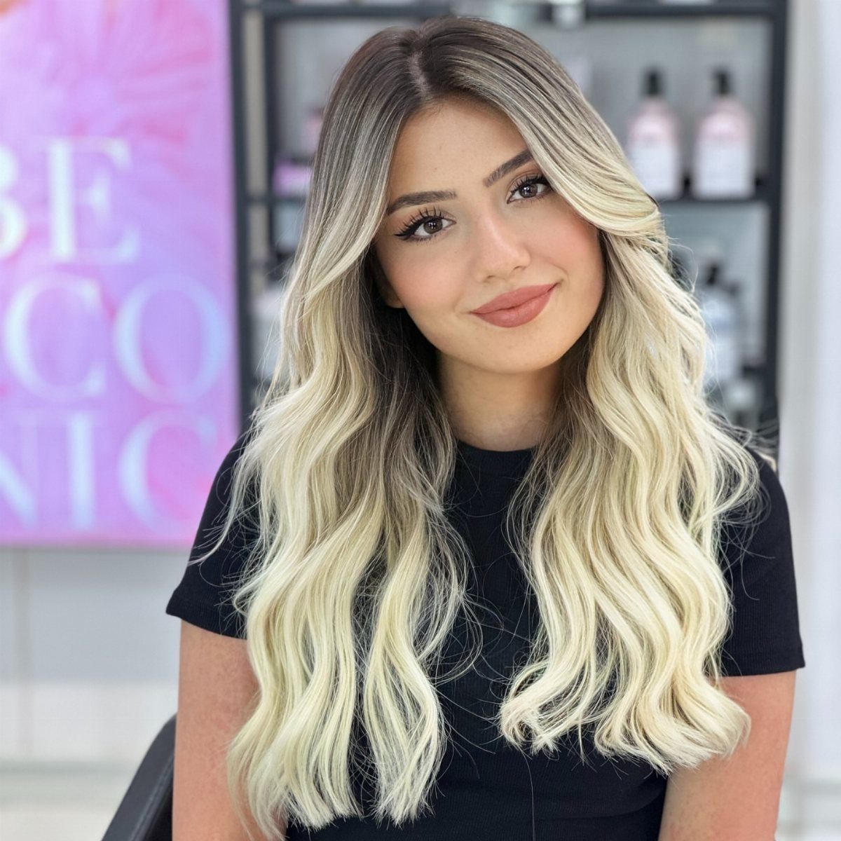 Woman with dark roots and wavy pale blonde ombre hair in a salon