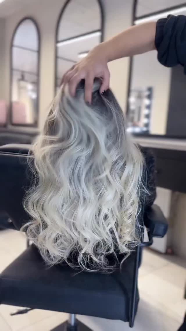 Wavy silver-blonde hair with dark roots displayed in a salon chair