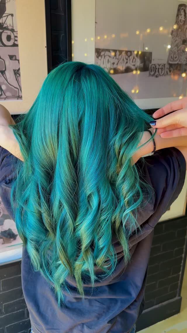 Long curled teal hair with darker roots being held at the side