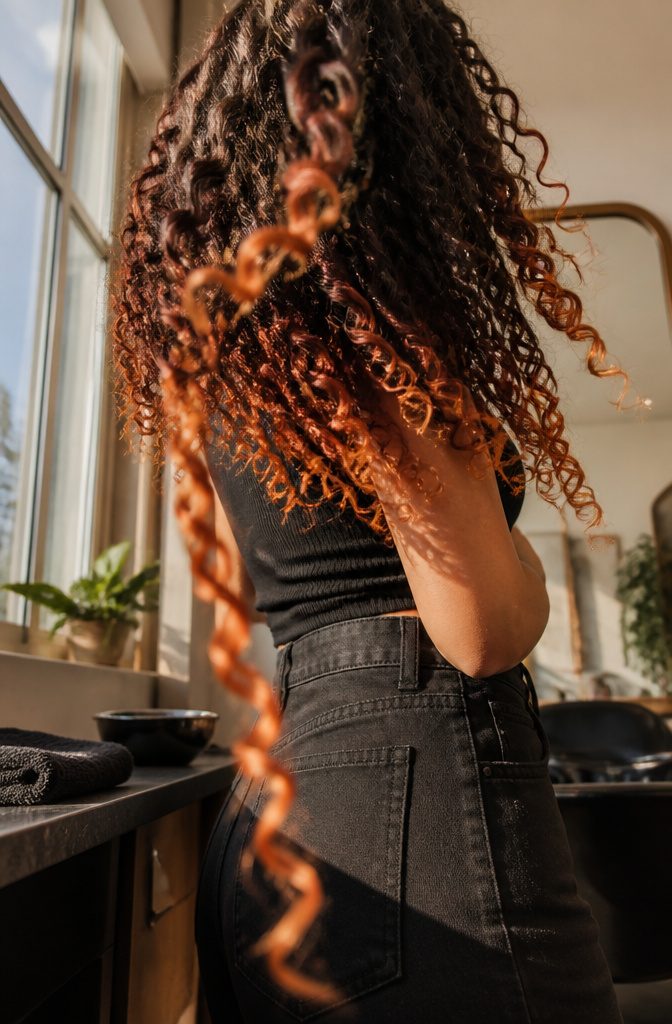 Voluminous defined curls fading from dark roots to reddish-orange ends